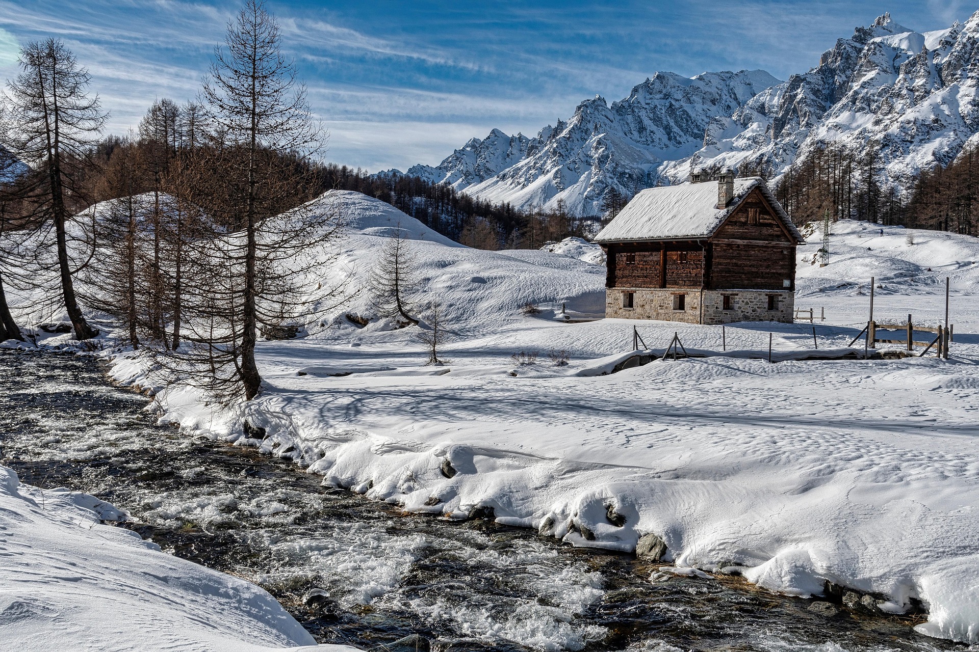 Chalet enneig&eacute; dans le Queyras en hiver avec rivi&egrave;re et montagnes en arri&egrave;re-plan